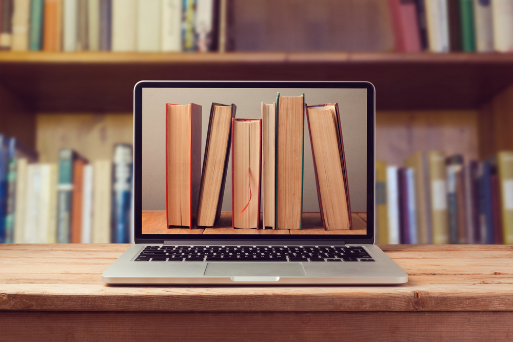 Computador portátil com livros a invocar a ideia de uma biblioteca digital