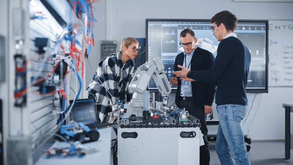 Três Cientistas junto a braço robótico.